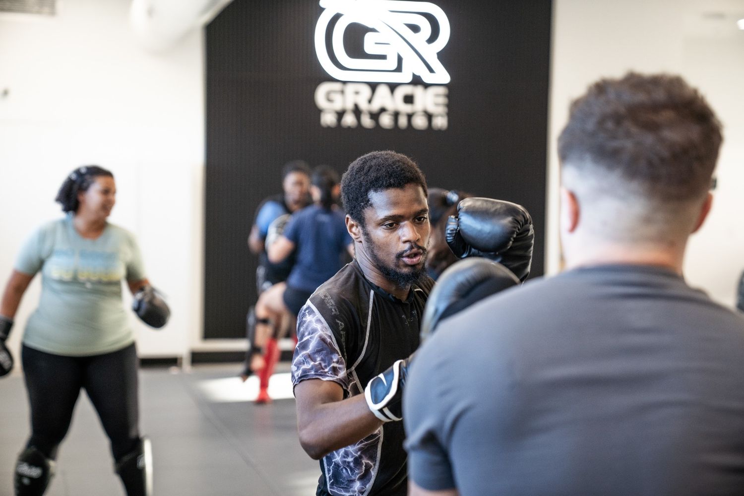 Students practicing partner striking drills and self-defense movements in a Raleigh kickboxing class.